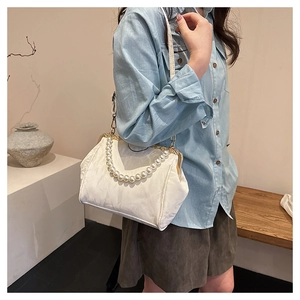 Close-up of cream shell bag featuring pleated fabric texture and large pearl handle detail