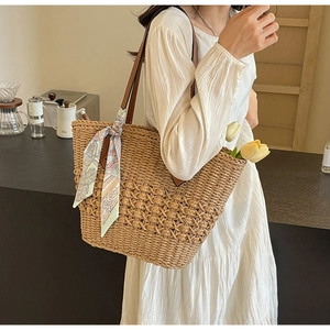 Detail view of woven straw tote bag with brown leather handles and floral scarf detail