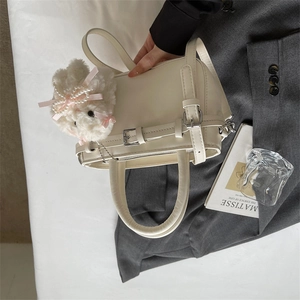 Detail of a minimalist cream tote bag with silver buckles and a cute plush bunny pendant