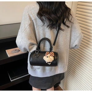 Black vintage cylinder pillow bag with plush bear charm worn over the shoulder