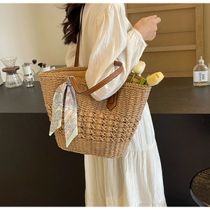Detail of woven straw tote bag with brown leather handles and a colorful floral scarf