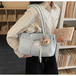 Detail of light blue patent leather tote bag with brown plush bear charm and bow