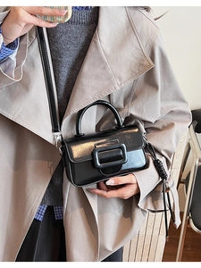 Detail of a black patent leather handbag with a large square buckle for urban commuting