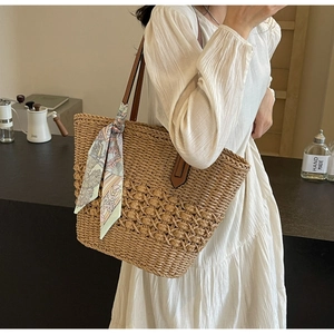 Close-up of woven straw tote bag with brown leather straps and decorative floral silk scarf
