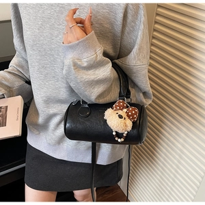 Detail of black leather cylindrical Boston bag featuring a plush puppy bag charm accessory