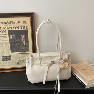 Detail of off-white tote bag with leather texture, metal buckle, and teddy bear charm