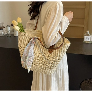 Detail of straw tote bag with brown leather handles and decorative floral silk scarf