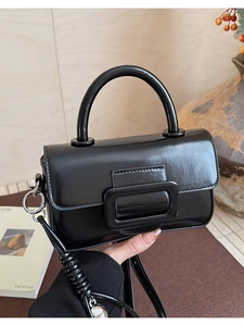 Close-up of elegant black leather square handbag with stylish round handle and decorative buckle