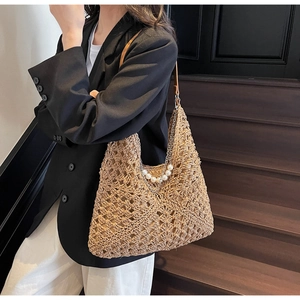 Detail of woven straw tote bag featuring elegant pearl and metal chain shoulder strap