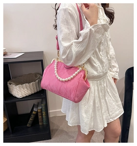Detailed view of pink pleated satin shell bag featuring large pearl handle and metal clasp