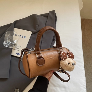 Detail of a brown leather boston bag with plush bear charm and embossed logo text