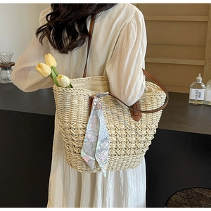 Close-up of woven straw tote bag featuring brown leather handles and decorative silk scarf