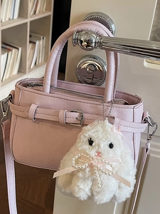 Pink minimalist handbag with plush bunny charm and shoulder strap hanging on door handle