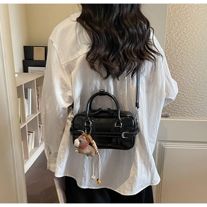 Detail of glossy black PU leather handbag with a brown pony charm and adjustable strap