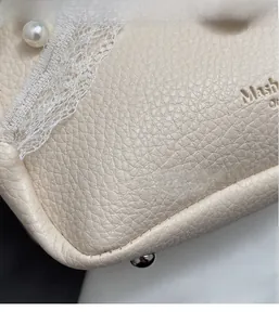 Close-up of beige lychee grain leather bag with white lace trim and pearl detail