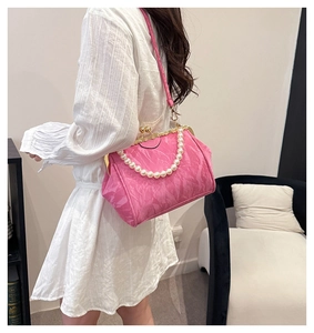 Pink shell bag with pearl handle and metal clasp shown on a model in a modern room