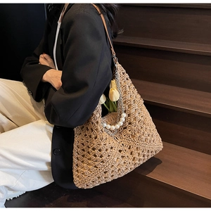 Detail view of woven straw tote bag featuring decorative pearl and silver metal chains