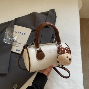 Detailed macro view of cream cylinder bag featuring brown trim and teddy bear charm