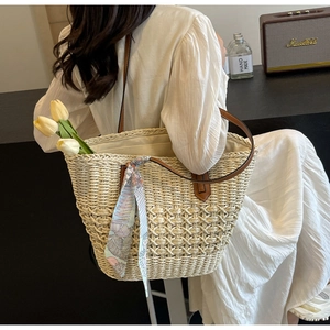 Close-up of handmade straw tote bag with floral scarf and brown leather handle