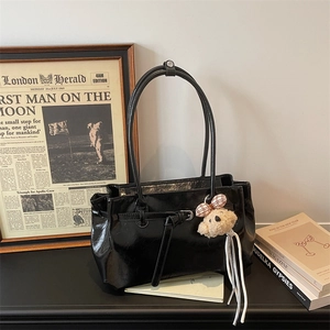 Detailed view of shiny black tote bag with long handles and cute plaid bow teddy bear charm