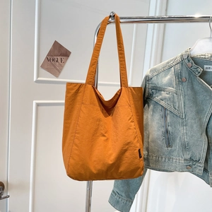 Detail view of large orange nylon tote bag with stitching and side woven label