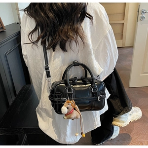 Detail of black glossy Boston bag featuring a cute plush horse charm and adjustable strap