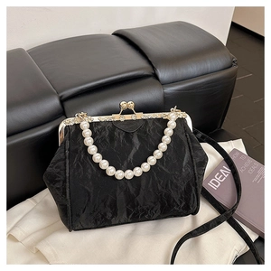 Close-up of black pleated fabric shell bag with pearl handle and ornate gold clasp