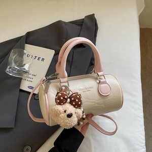 Detail view of cream white cylinder bag with pink handles and cute plush bear charm