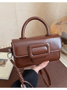 Detail of a deep brown glossy square handbag with an elegant wrapped strap and buckle