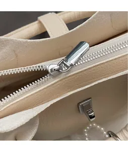 Detail of silver smooth zipper slider and pebbled leather texture on beige bucket bag