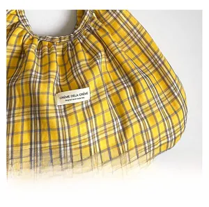 Detail of yellow checkered fabric bag featuring pleated texture and woven label