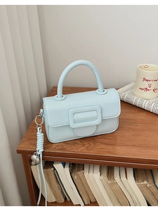Detail view of light blue crossbody bag with square buckle and woven heart pendant strap