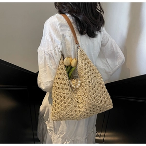 Detailed macro view of beige hollow crochet straw bag with leather strap and pearl charm