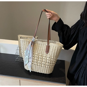 Detailed macro view of woven straw tote bag with leather handle and silk scarf accessory