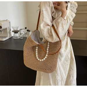Detail of handmade woven straw tote bag with pearl handle and brown leather strap