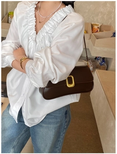 Close-up of a dark brown glossy leather underarm bag with a golden square buckle