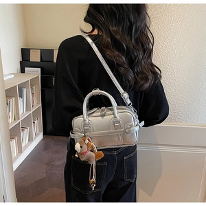 Silver metallic Boston bag featuring a plush horse charm and adjustable strap detail