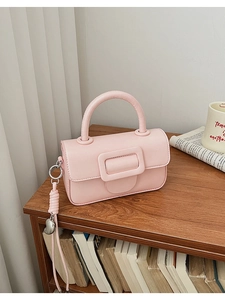 Detail of light pink mini handbag with large square buckle and heart pendant on bookshelf