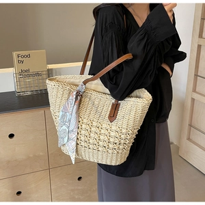 Detail of hand-woven straw tote with leather handles and decorative silk scarf