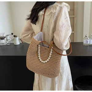 Detail of straw woven tote bag featuring faux pearl handles and brown leather strap
