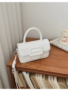 Detailed view of a white leather square handbag with a large buckle on a wooden desk