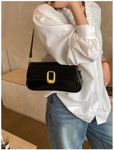 Side view of a glossy black underarm bag with a decorative gold rectangular buckle