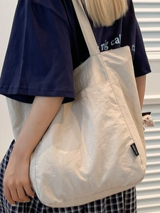 Minimalist beige nylon tote bag with black label shown on model's shoulder in casual style
