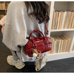 Red patent leather Boston bag with a horse charm shown in an atmospheric indoor setting