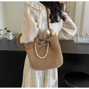 Artistic handmade straw tote bag featuring pearl handles and leather strap on a model