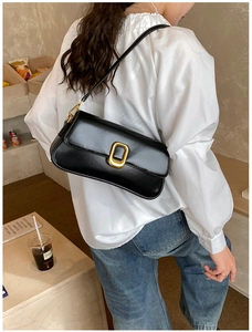 Detail view of a black glossy leather baguette bag with a stylish gold oval metal buckle