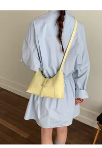 Side view of a creamy yellow shoulder bag with leather strap buckle on a model