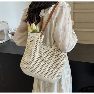 Detail of woven cotton tote bag featuring white faux pearl strap and brown leather handle