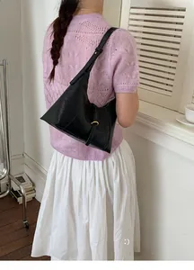Detail of minimalist black crescent bag with golden buckle on elegant knit outfit