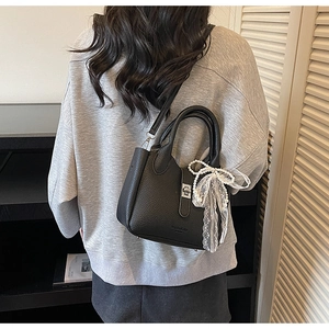 Detail of black litchi leather bucket bag featuring silver lock and pearl lace bow